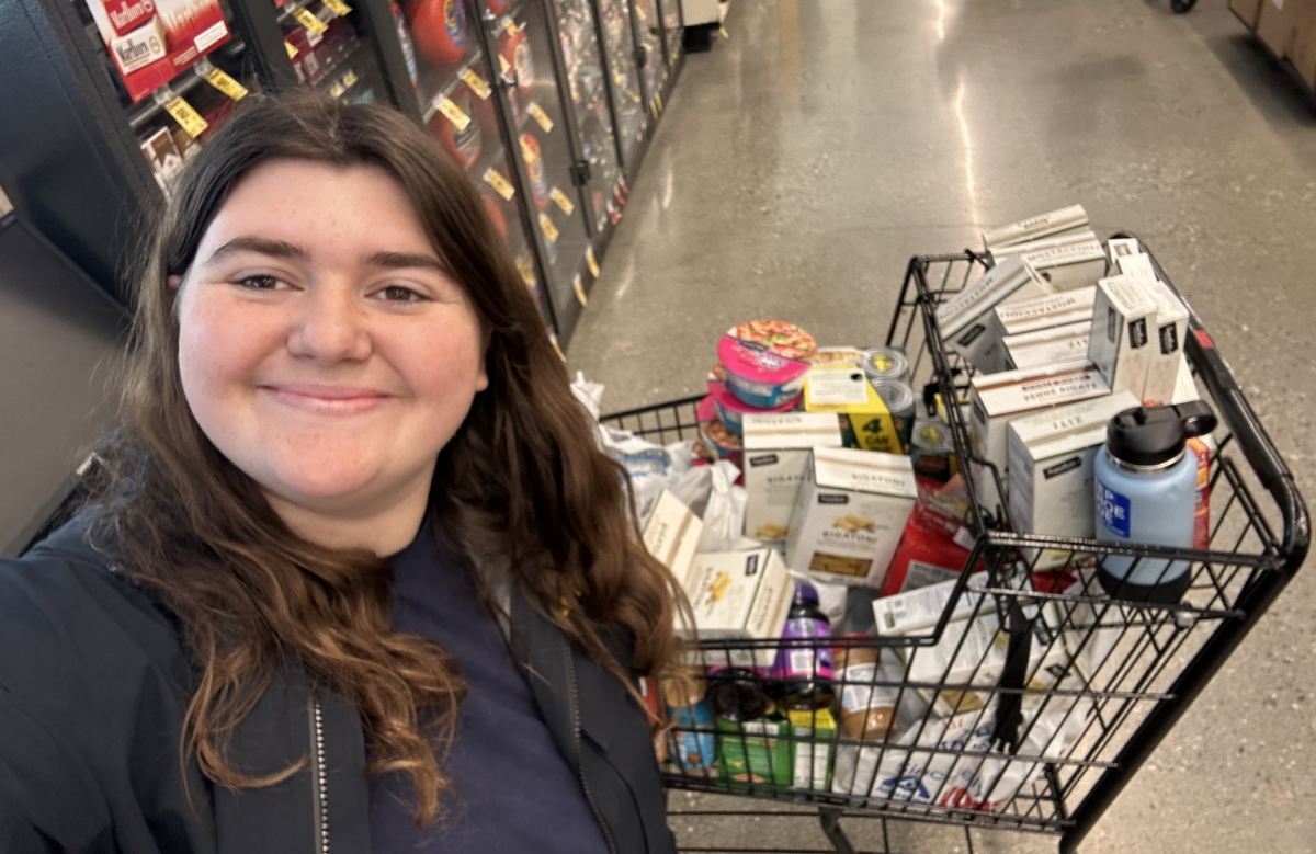 A selfie of me with a cart full of pasta, cans, and other food items.